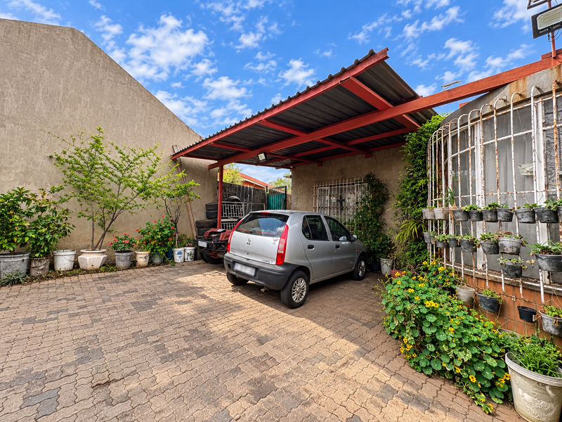 A paved rear courtyard area featuring a covered carport structure and security-fitted windows, providing functional outdoor space.