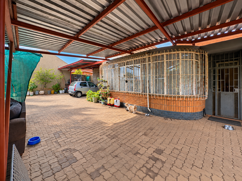 A covered outdoor patio area featuring a corrugated metal roof, brick facade, and security bars, providing a functional space for outdoor activities.