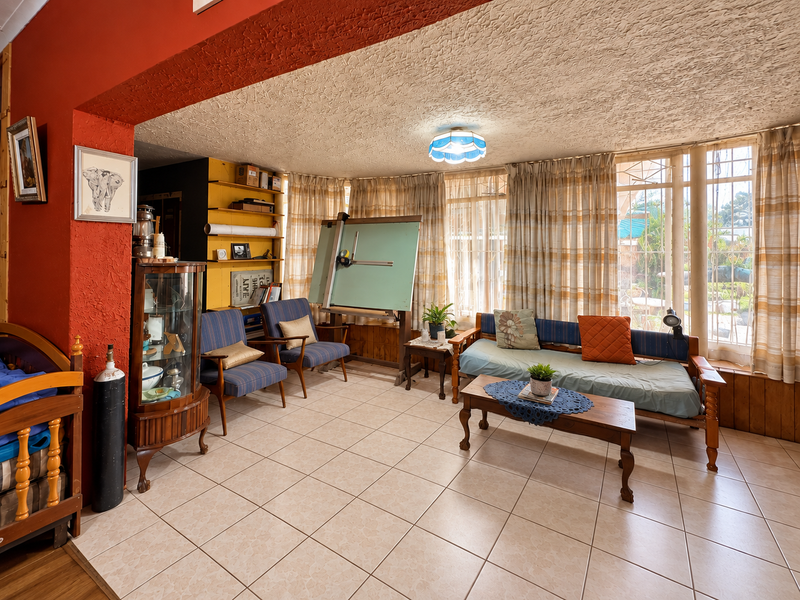A living area featuring tiled flooring, textured ceilings, and built-in shelving, with large windows providing natural light.