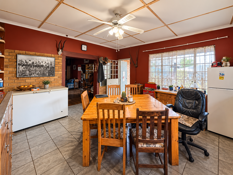 Dining area featuring tiled flooring, exposed brick accent wall, and a ceiling fan, offering a functional space with potential for modern updates.