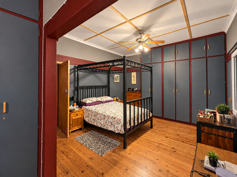 Spacious bedroom featuring extensive floor-to-ceiling built-in cabinetry, polished timber flooring, and a decorative ceiling with a central fan.