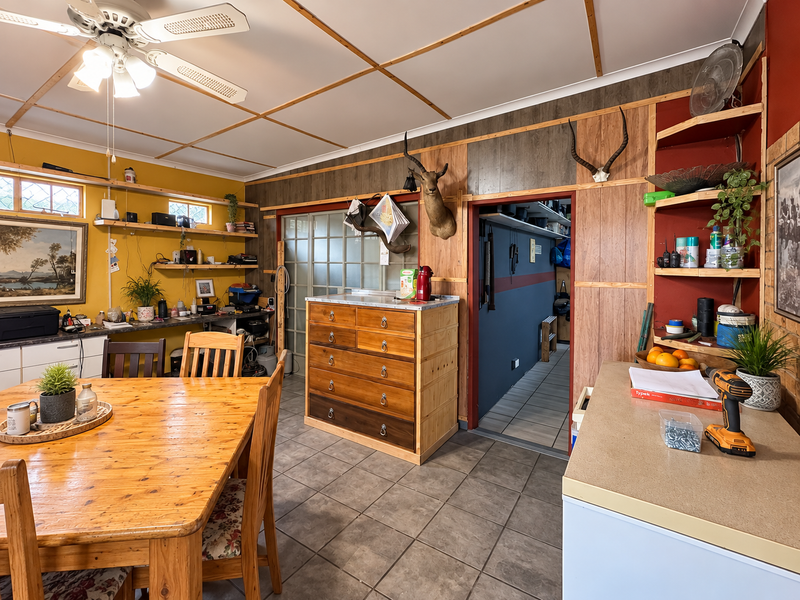 Open plan living area featuring tiled flooring, ceiling fan, and built-in shelving with wood paneling accents, offering potential for modernization.