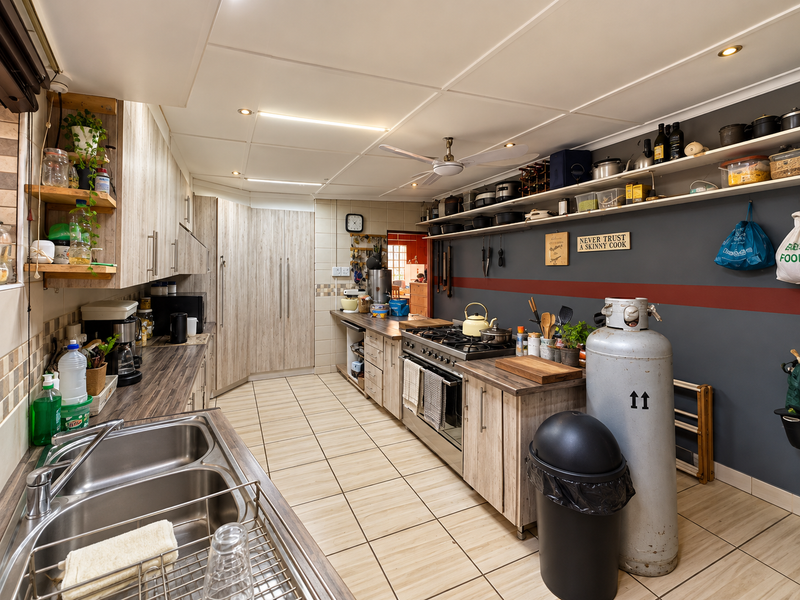 A functional kitchen featuring wood-look cabinetry, laminate countertops, a gas stove, and tiled flooring with ample open shelving for storage.