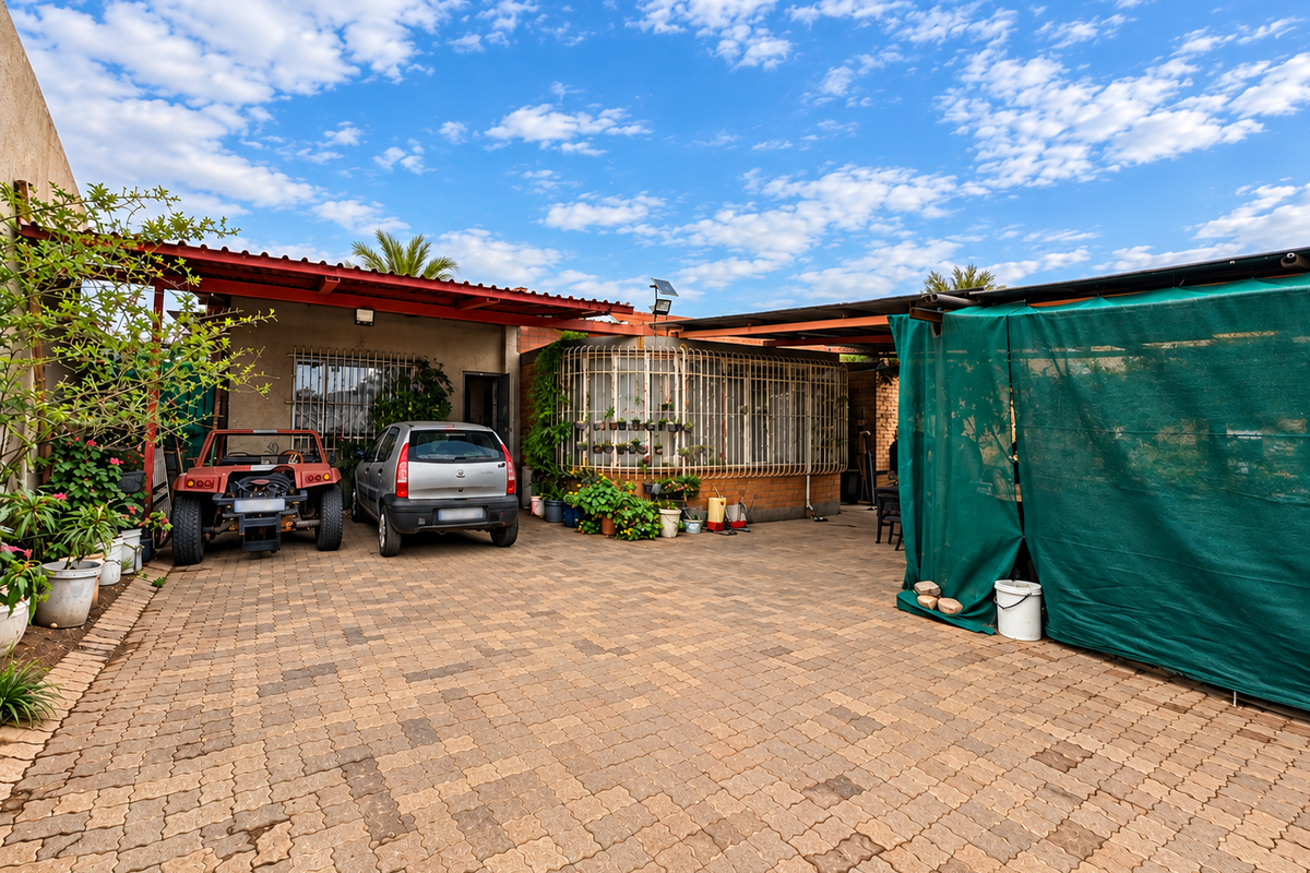 A paved rear courtyard area featuring a covered patio structure, security bars on windows, and brick walling.