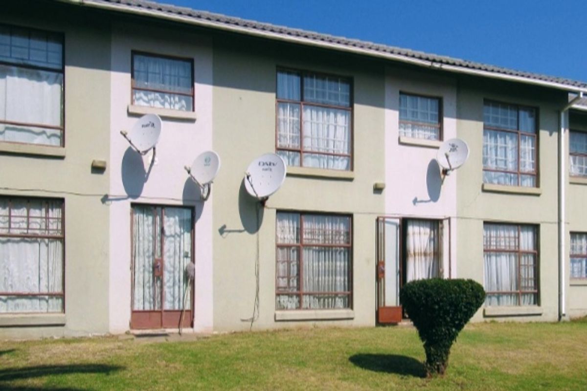Rear elevation of a multi-story apartment building featuring multiple satellite dishes, security gates, and standard window frames overlooking a communal lawn area.