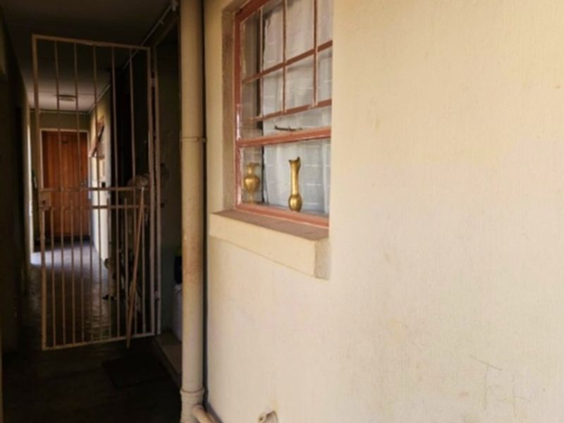 A narrow apartment hallway featuring a security gate and a window, showing signs of wear on the wall surfaces.