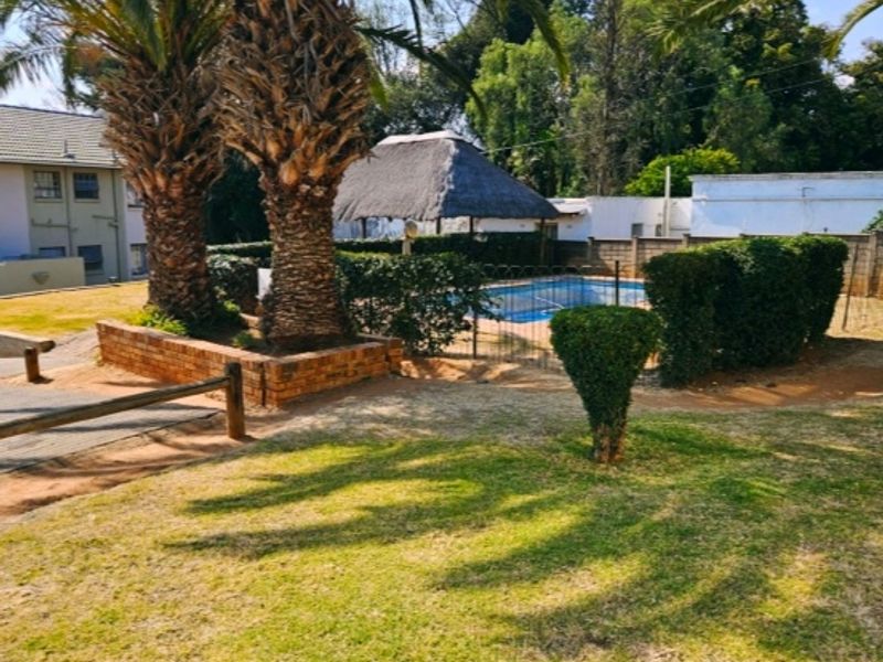 Communal outdoor area featuring a swimming pool, a thatched lapa, and established garden landscaping with mature palm trees.