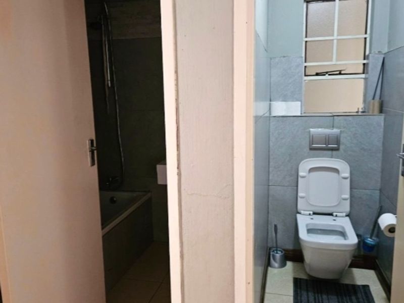 A functional bathroom featuring a wall-mounted toilet and a separate bathtub area, showing signs of wear and ceiling water damage requiring maintenance.