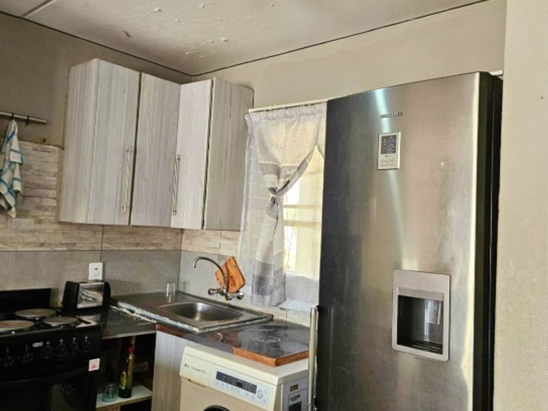 Compact kitchen featuring built-in cabinetry, stainless steel sink, and integrated appliances, showing signs of ceiling wear requiring maintenance.