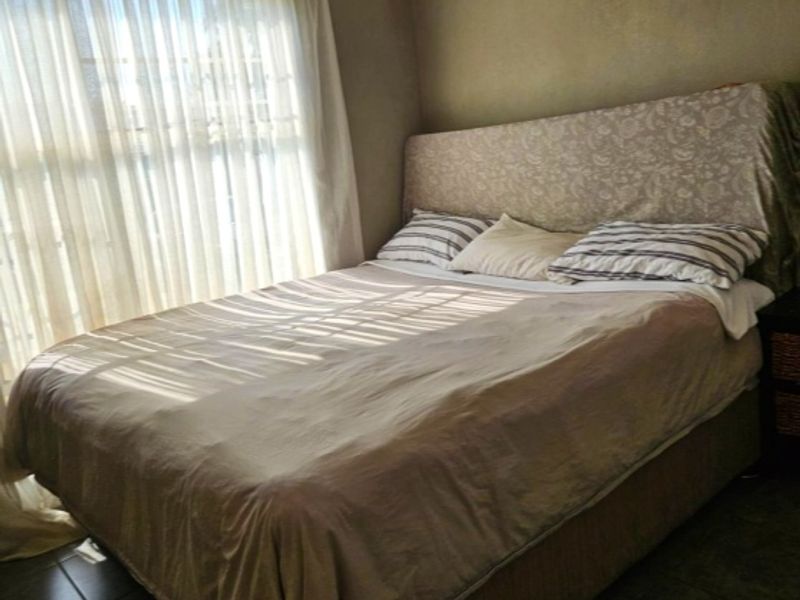 A bedroom featuring tiled flooring and a large window with sheer curtains, providing natural light.