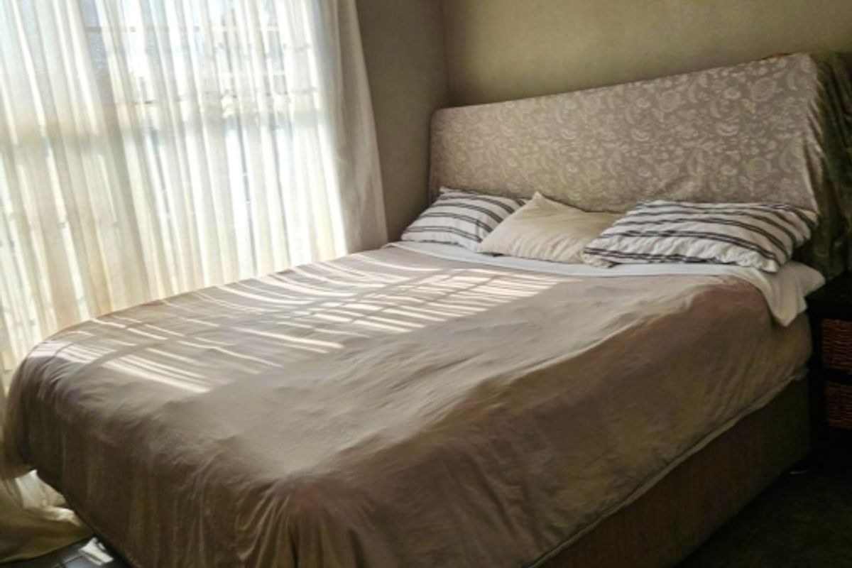A bedroom featuring tiled flooring and a large window with sheer curtains, providing natural light.