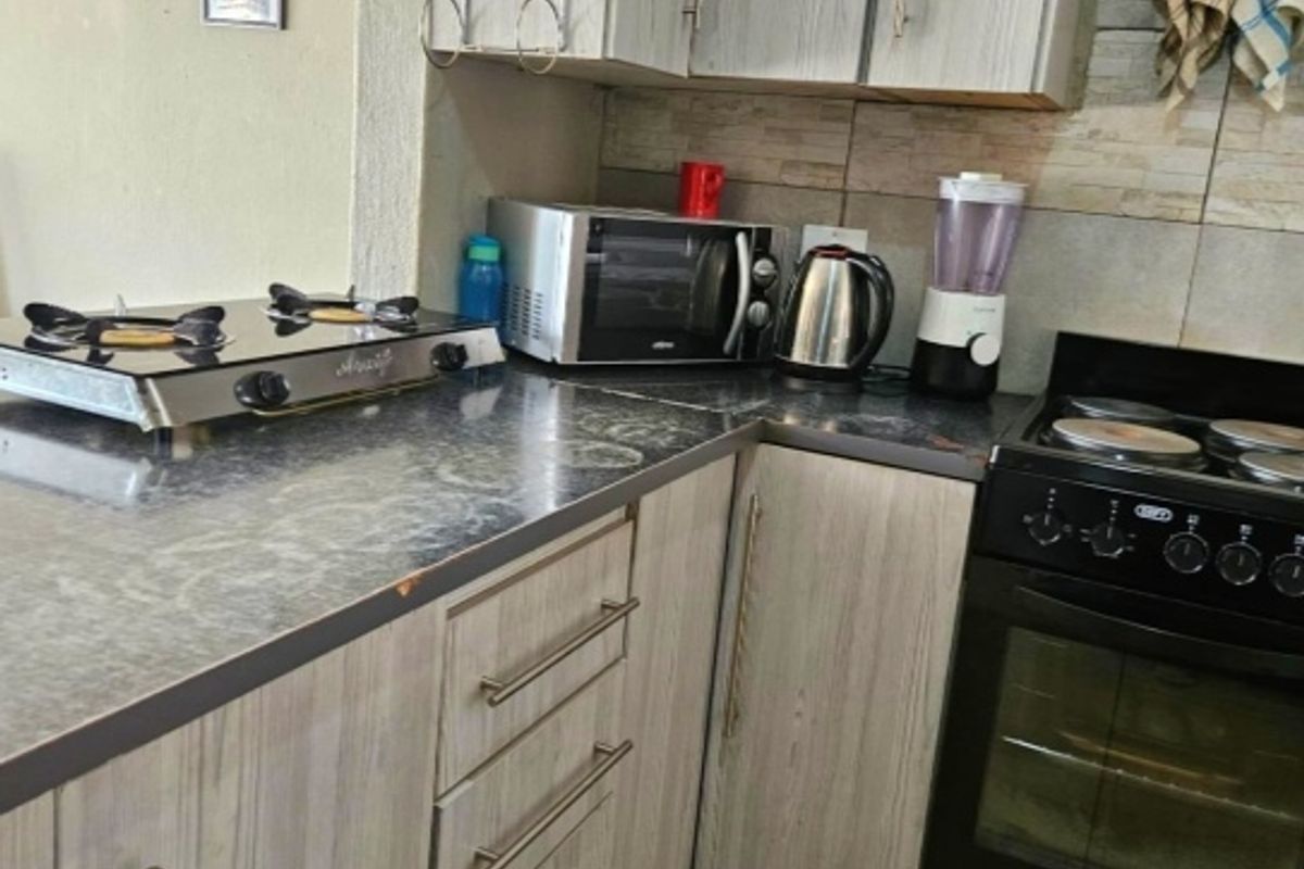 A functional kitchen featuring wood-grain laminate cabinetry, a stone-look countertop, tiled backsplash, and a freestanding oven with a gas hob.
