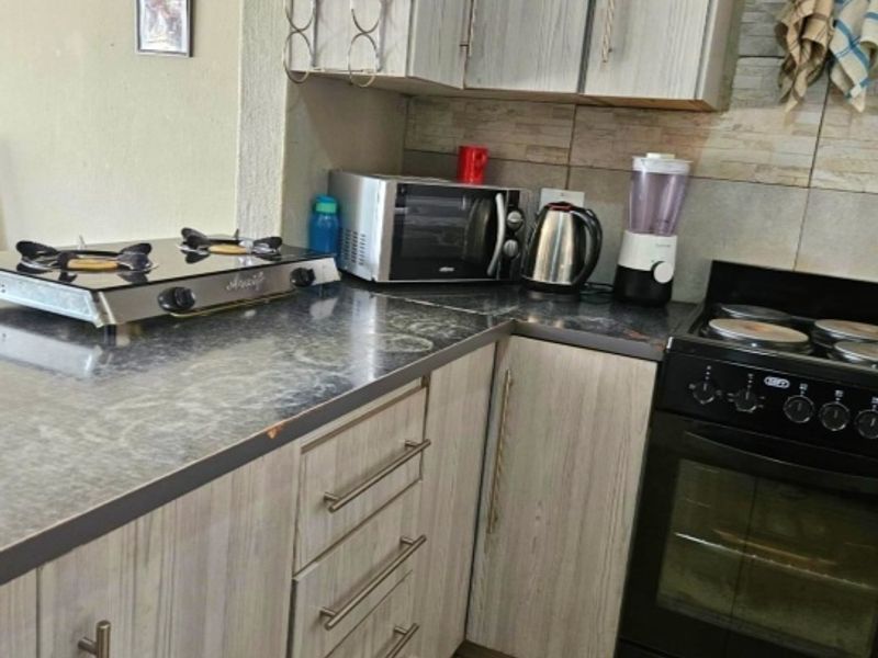 A functional kitchen featuring wood-grain laminate cabinetry, a stone-look countertop, tiled backsplash, and a freestanding oven with a gas hob.