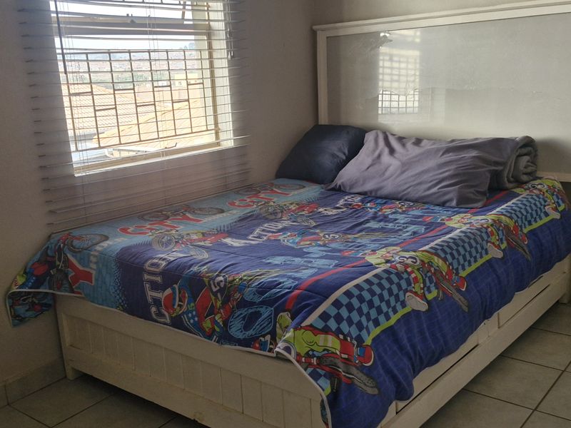 A functional bedroom featuring tiled flooring, a window with venetian blinds, and a built-in wardrobe.