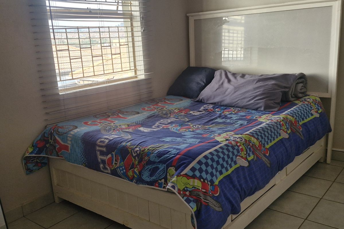 A functional bedroom featuring tiled flooring, a window with venetian blinds, and a built-in wardrobe.