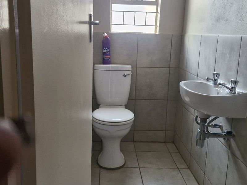 A compact guest bathroom featuring a wall-mounted basin, standard toilet, and neutral tiled finishes with security bars on the window.