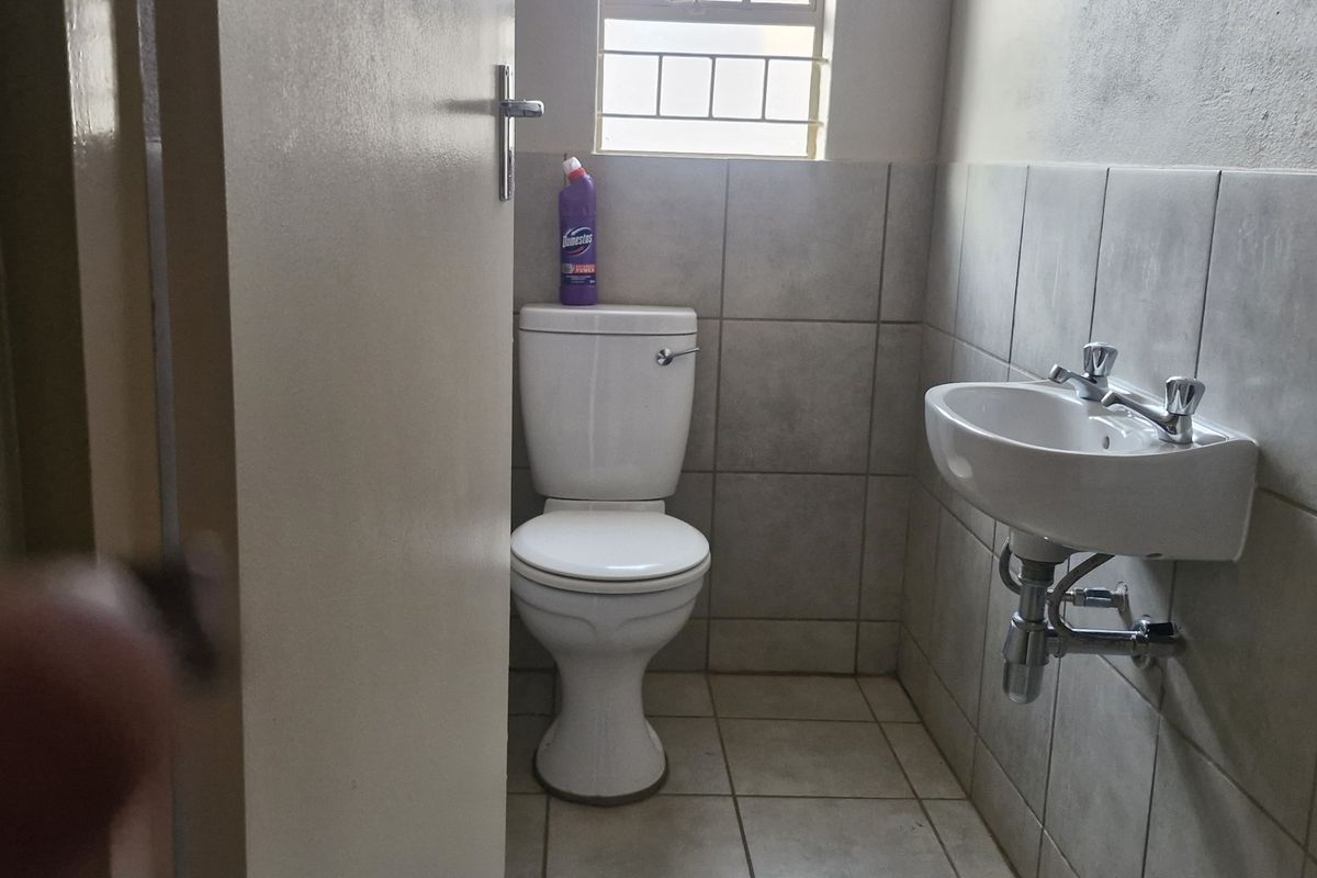 A compact guest bathroom featuring a wall-mounted basin, standard toilet, and neutral tiled finishes with security bars on the window.