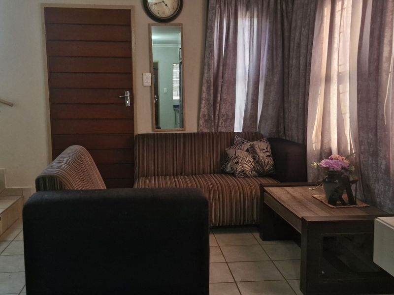 A living room area featuring tiled flooring, a staircase with a metal railing, and a wooden door, providing a functional and accessible layout.