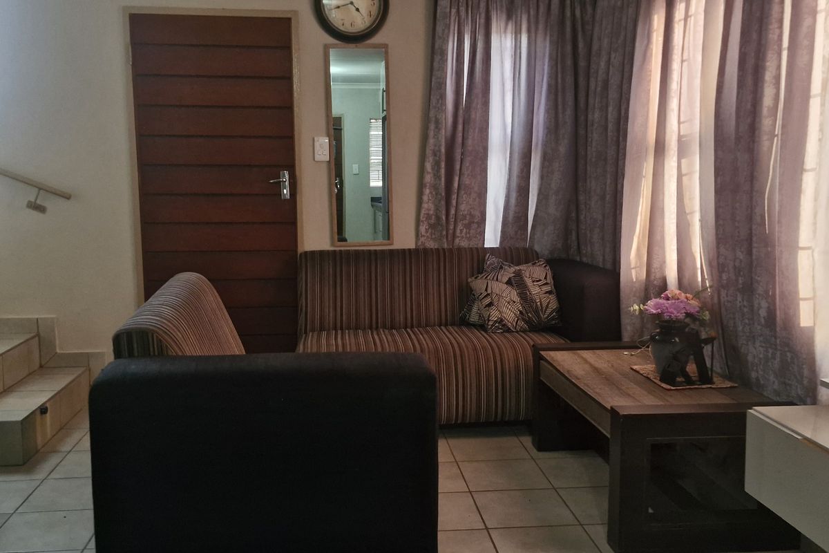 A living room area featuring tiled flooring, a staircase with a metal railing, and a wooden door, providing a functional and accessible layout.
