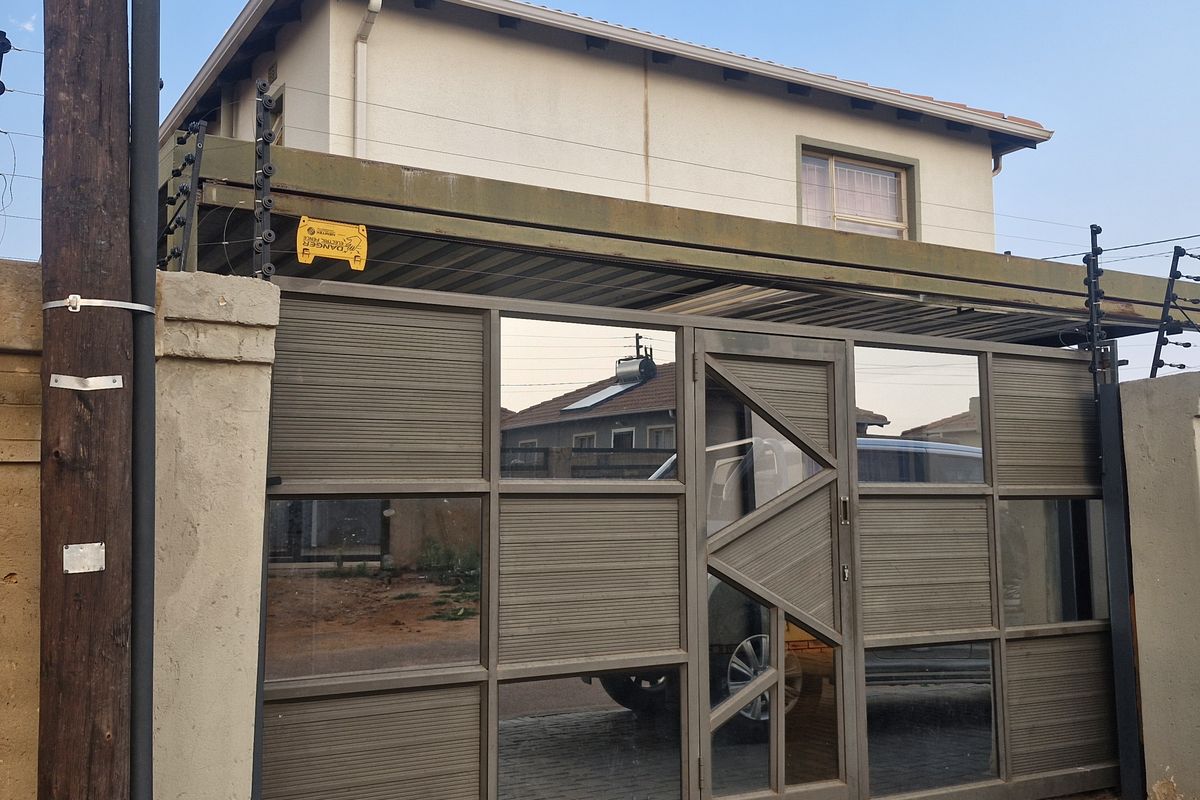 Front view of the property featuring a modern metal sliding gate, integrated carport, and perimeter masonry wall with installed electric security fencing.