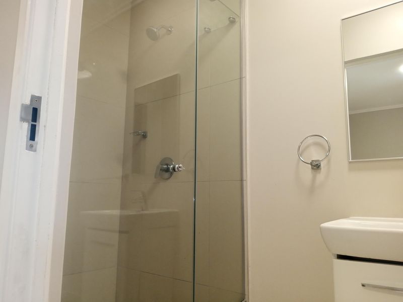 A clean, modern bathroom featuring a glass-enclosed shower, wall-mounted vanity basin, and a simple mirror, presenting a functional and well-maintained space.