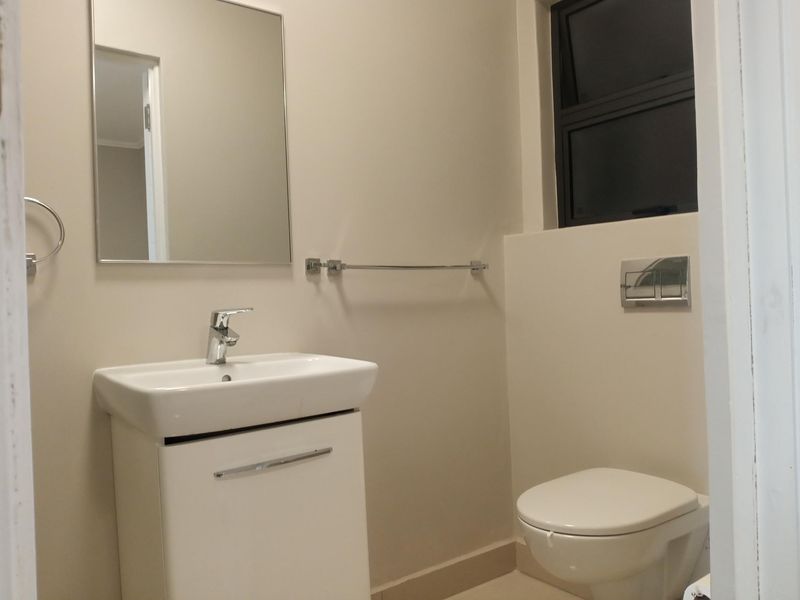 A clean, modern bathroom featuring a wall-hung toilet with a concealed cistern, a vanity basin, and a wall-mounted mirror.