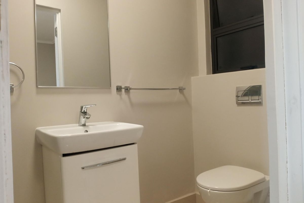 A clean, modern bathroom featuring a wall-hung toilet with a concealed cistern, a vanity basin, and a wall-mounted mirror.