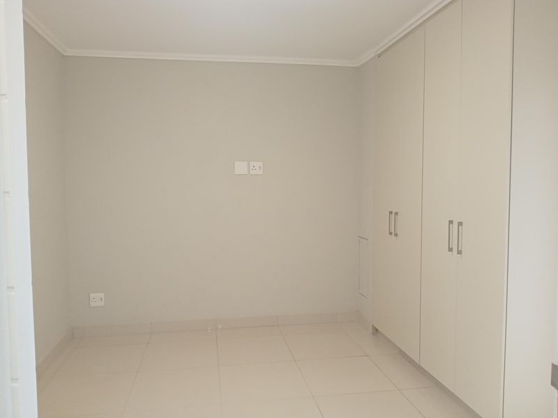 A clean, empty bedroom featuring neutral tiled flooring and ample built-in cupboard storage space.