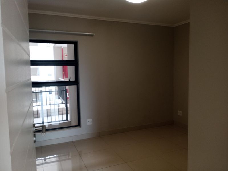 A clean, empty bedroom featuring neutral wall tones, tiled flooring, and an aluminium-framed window providing natural light.