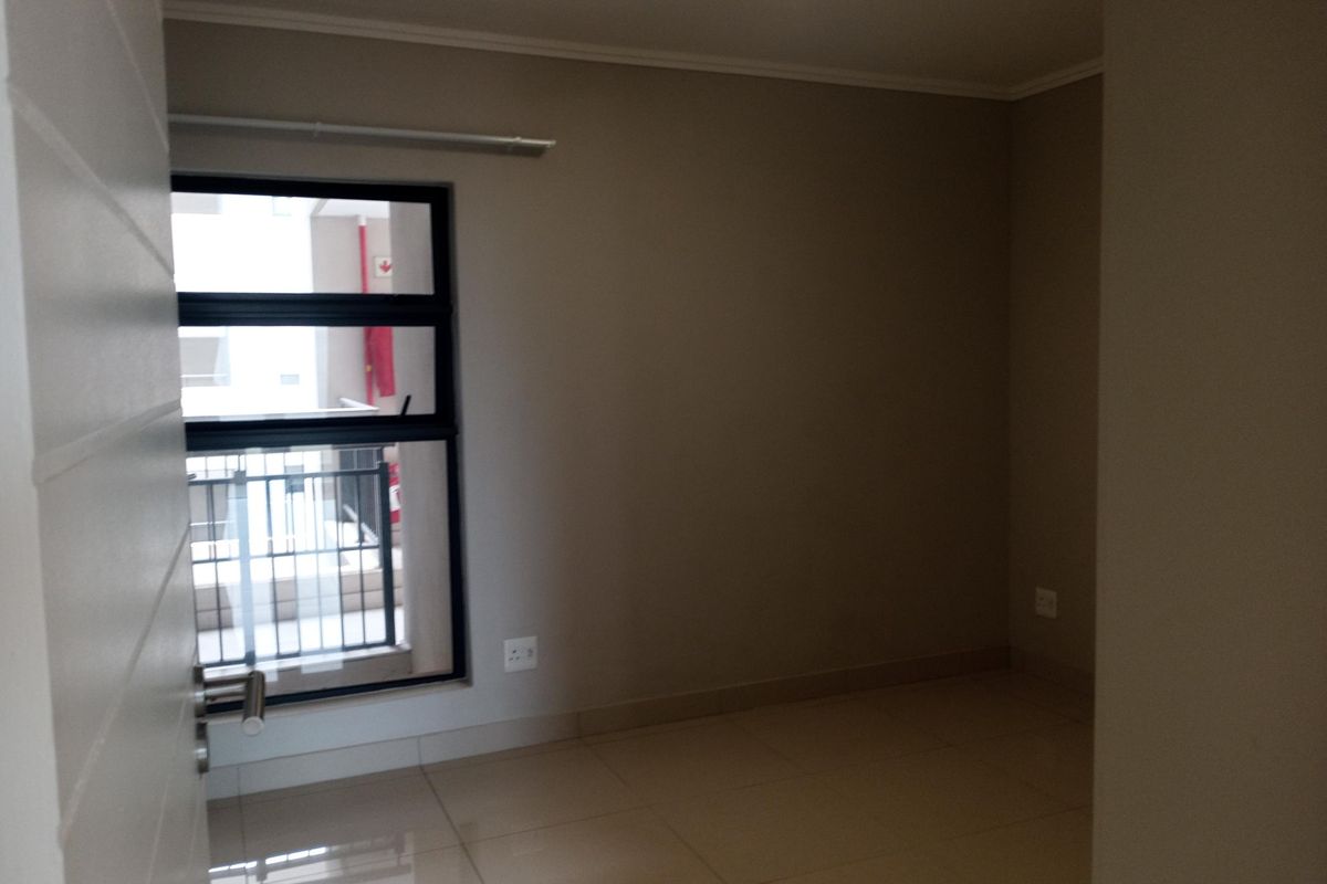 A clean, empty bedroom featuring neutral wall tones, tiled flooring, and an aluminium-framed window providing natural light.