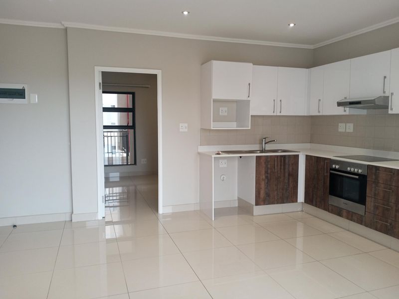 Modern open-plan kitchen featuring white and wood-grain cabinetry, integrated oven and hob, and sleek tiled flooring in a bright, neutral living space.