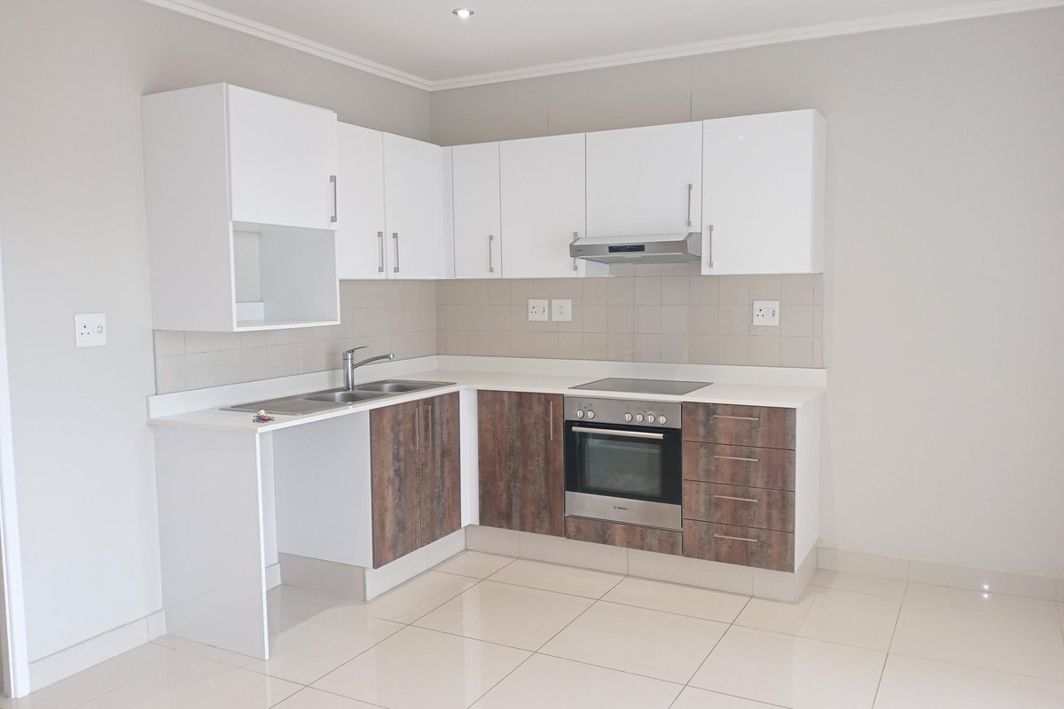 A clean, modern kitchen featuring white upper cabinets, wood-finish lower cabinetry, integrated oven and hob, and neutral tiled flooring.