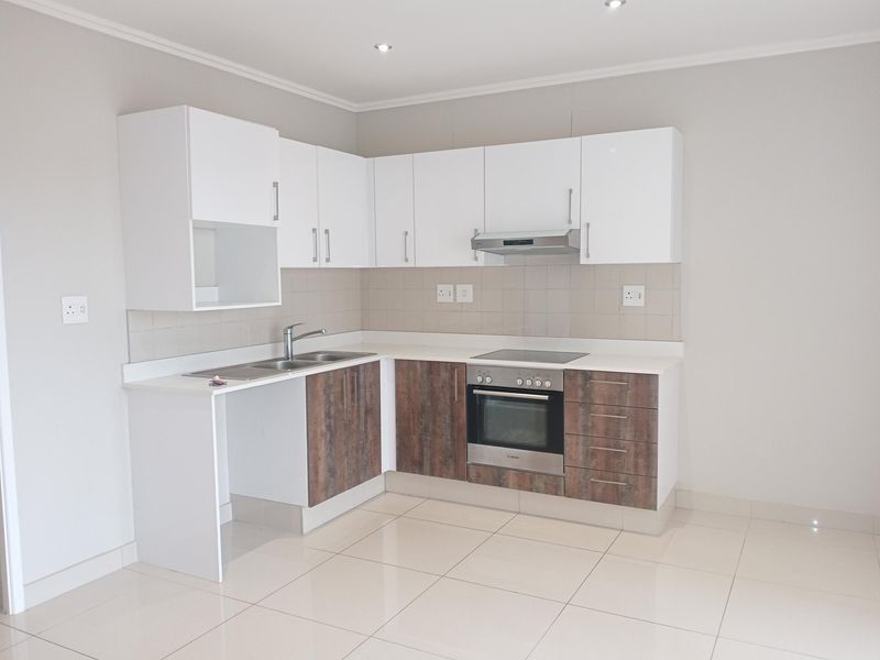 A clean, modern kitchen featuring white upper cabinets, wood-finish lower cabinetry, integrated oven and hob, and neutral tiled flooring.