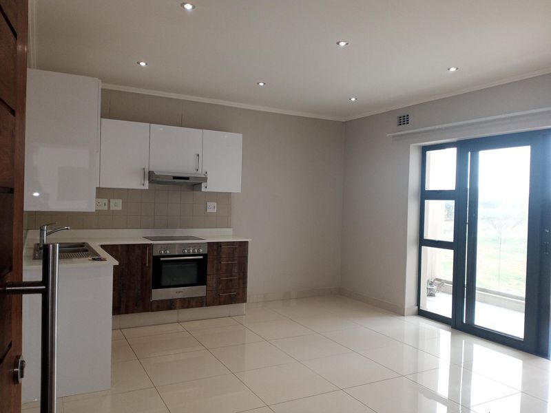Modern open-plan kitchen and living area featuring sleek cabinetry, integrated appliances, tiled flooring, and direct access to a balcony through sliding glass doors.