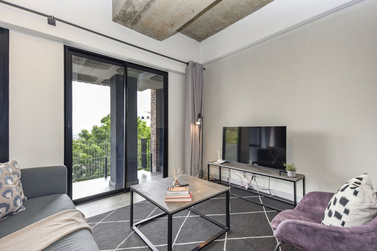 Modern living room featuring an exposed concrete ceiling, laminate flooring, and large sliding glass doors opening onto a private balcony.