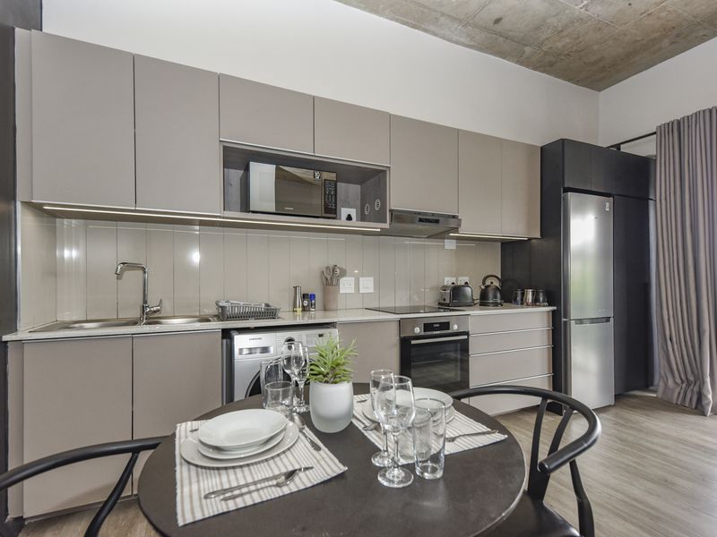Modern open-plan kitchen featuring sleek cabinetry, stone countertops, integrated appliances, and an exposed concrete ceiling, seamlessly flowing into the dining area.