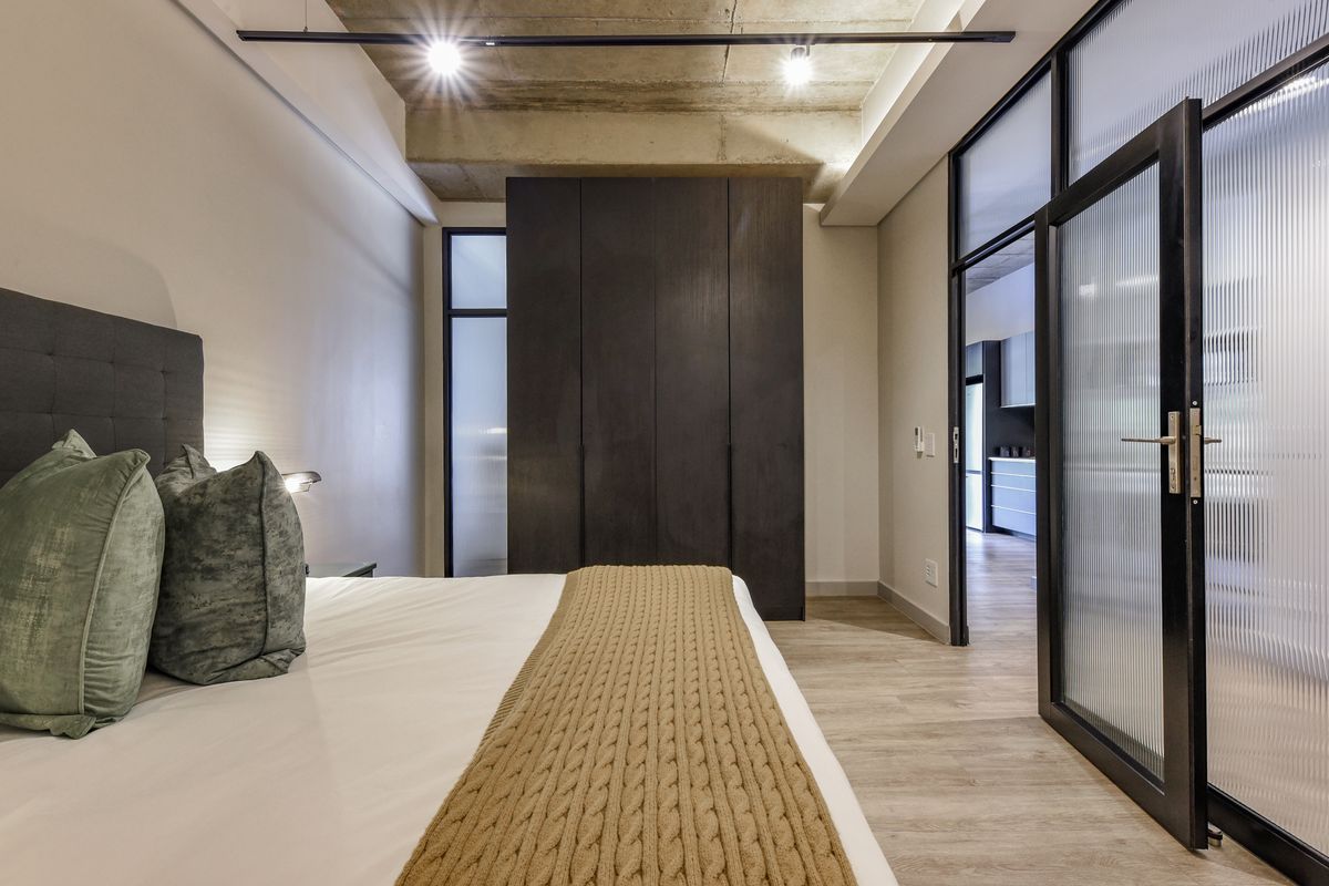 Modern bedroom featuring an exposed concrete ceiling, built-in dark wood cabinetry, and a stylish fluted glass door leading to the adjacent living space.