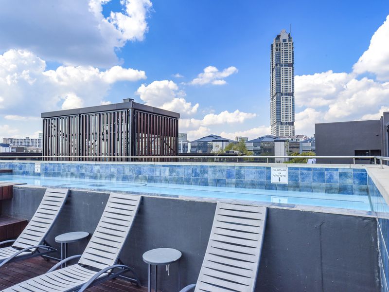 Rooftop swimming pool area featuring timber decking, tiled pool surround, and modern metal railings with expansive city skyline views.