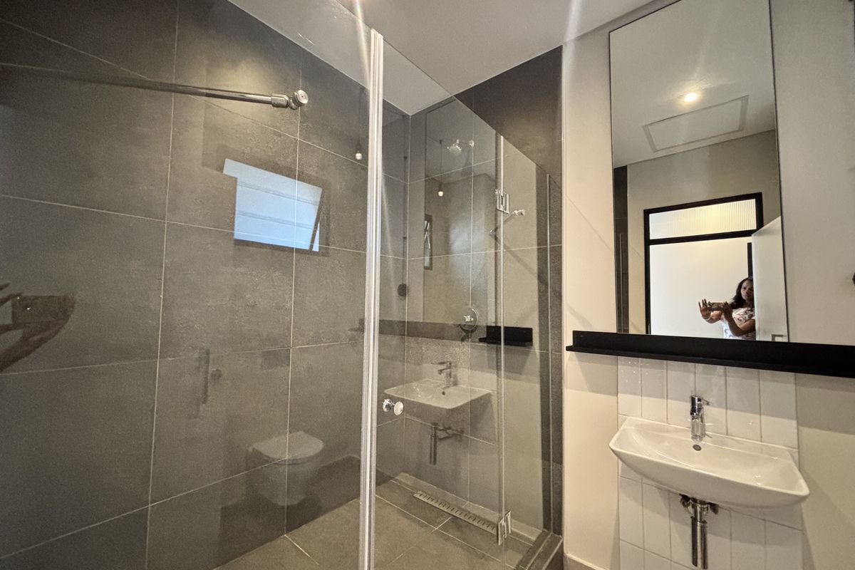 Modern bathroom featuring a glass-enclosed walk-in shower, wall-mounted basin, and large mirror with contemporary grey and white tiling.