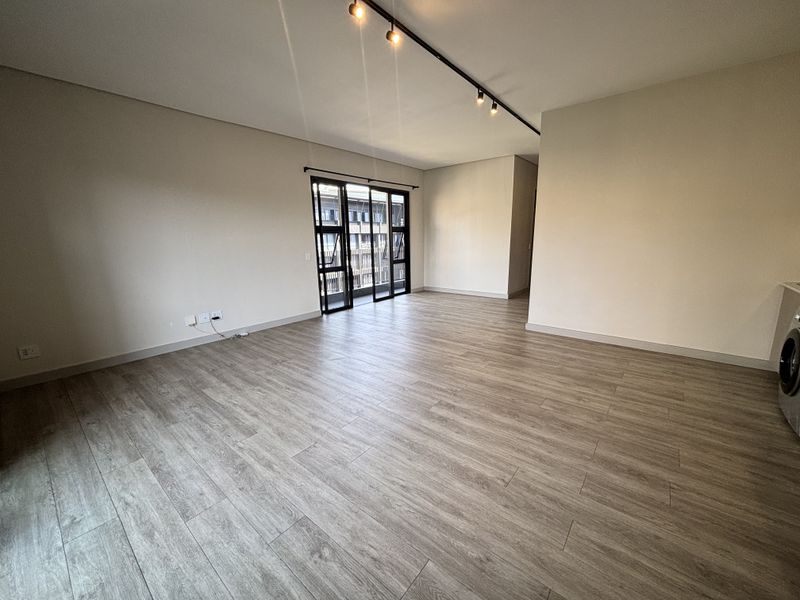 Spacious open-plan living area featuring modern laminate flooring, track lighting, and large black-framed sliding doors leading to an outdoor space.