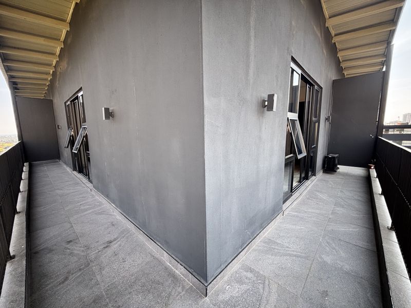 A spacious wrap-around balcony featuring tiled flooring, metal balustrades, and modern sliding glass door access to the apartment interior.