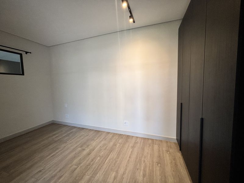 A clean, modern bedroom featuring light wood-look laminate flooring, neutral walls, and dark built-in cupboards with minimalist hardware.