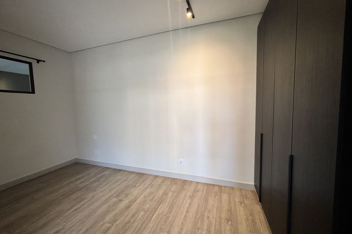 A clean, modern bedroom featuring light wood-look laminate flooring, neutral walls, and dark built-in cupboards with minimalist hardware.