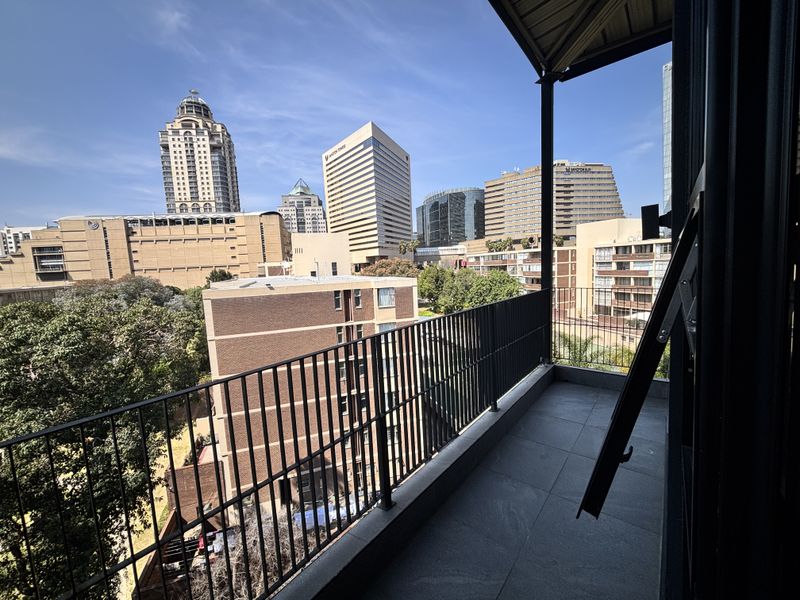 A private balcony featuring tiled flooring and a metal balustrade, offering expansive urban views of the surrounding city skyline.