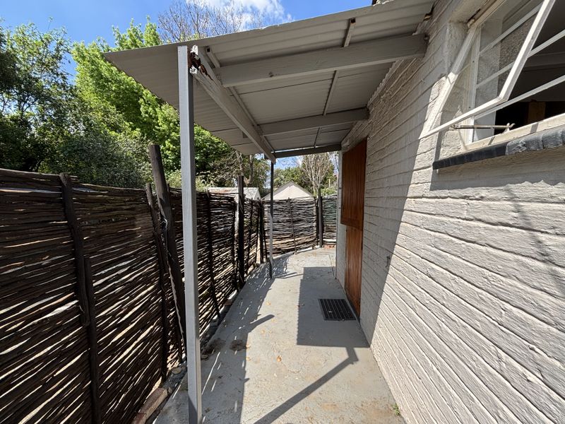 A covered outdoor patio area featuring a corrugated metal roof, painted brick exterior, and concrete flooring, providing a functional transition space.
