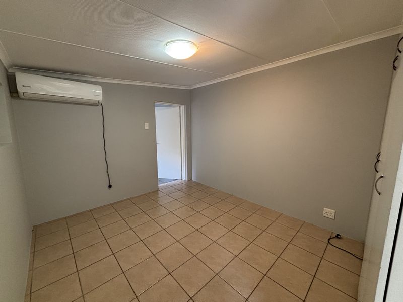 A clean, empty bedroom featuring tiled flooring, a wall-mounted air conditioning unit, and built-in storage cabinetry.