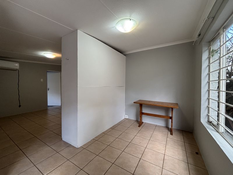 A spacious, tiled living area featuring a partition wall, split-system air conditioning, and large windows with security bars, offering a neutral blank canvas.