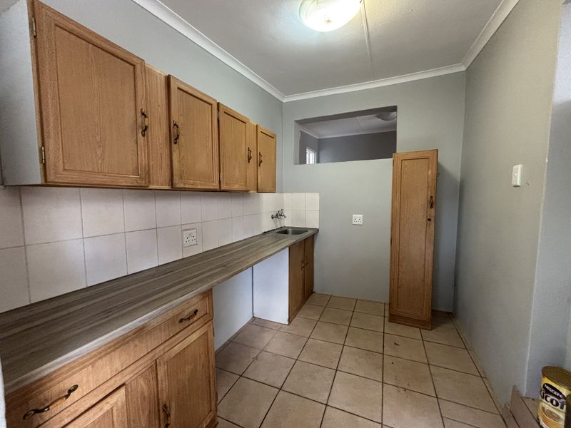 A functional scullery area featuring wooden cabinetry, a laminate countertop with an integrated sink, and tiled flooring.