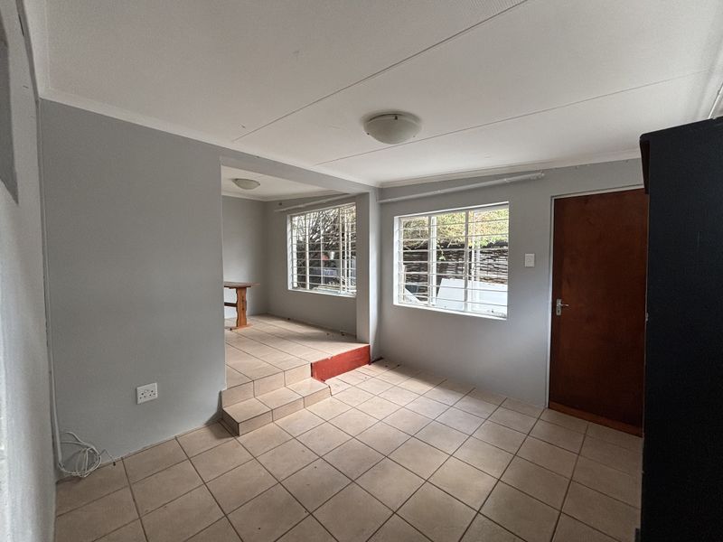 An open-plan living area featuring tiled flooring, a raised floor section, and security bars on the windows, offering a functional and neutral space.