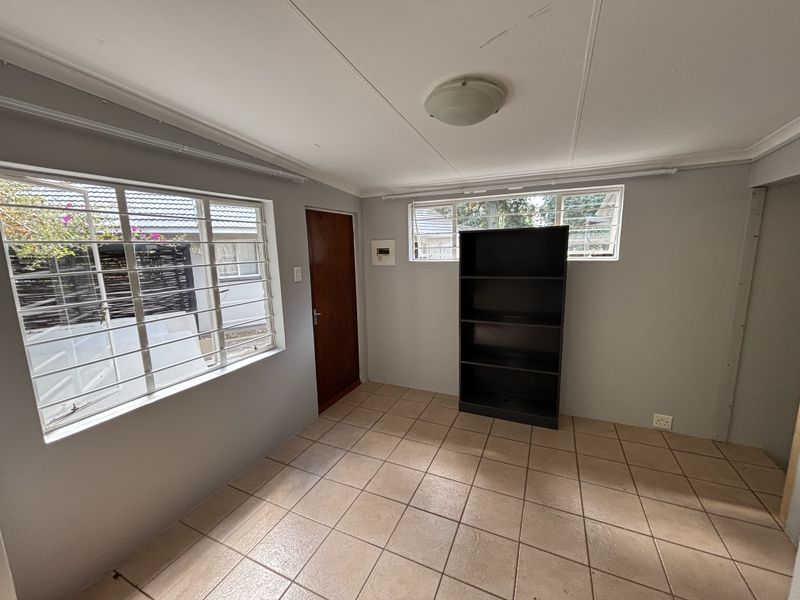 A simple, empty bedroom featuring tiled flooring, security bars on the windows, and a neutral wall finish, ready for personalization.